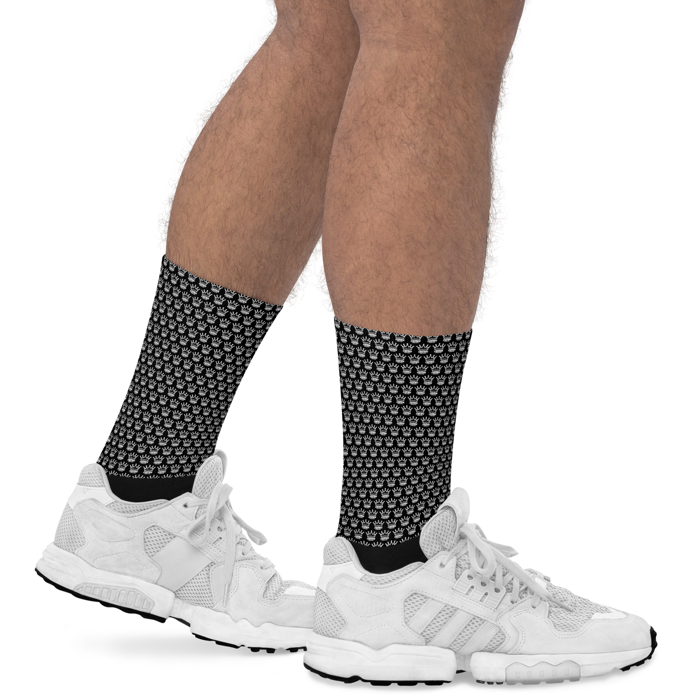 Only the legs are visible, showing light brown skin and some leg hair, wearing Crown Pickleball - Checkered Crown (Black) crew socks with white sneakers on a white background. The black socks feature a checkered pattern and reach mid-calf.