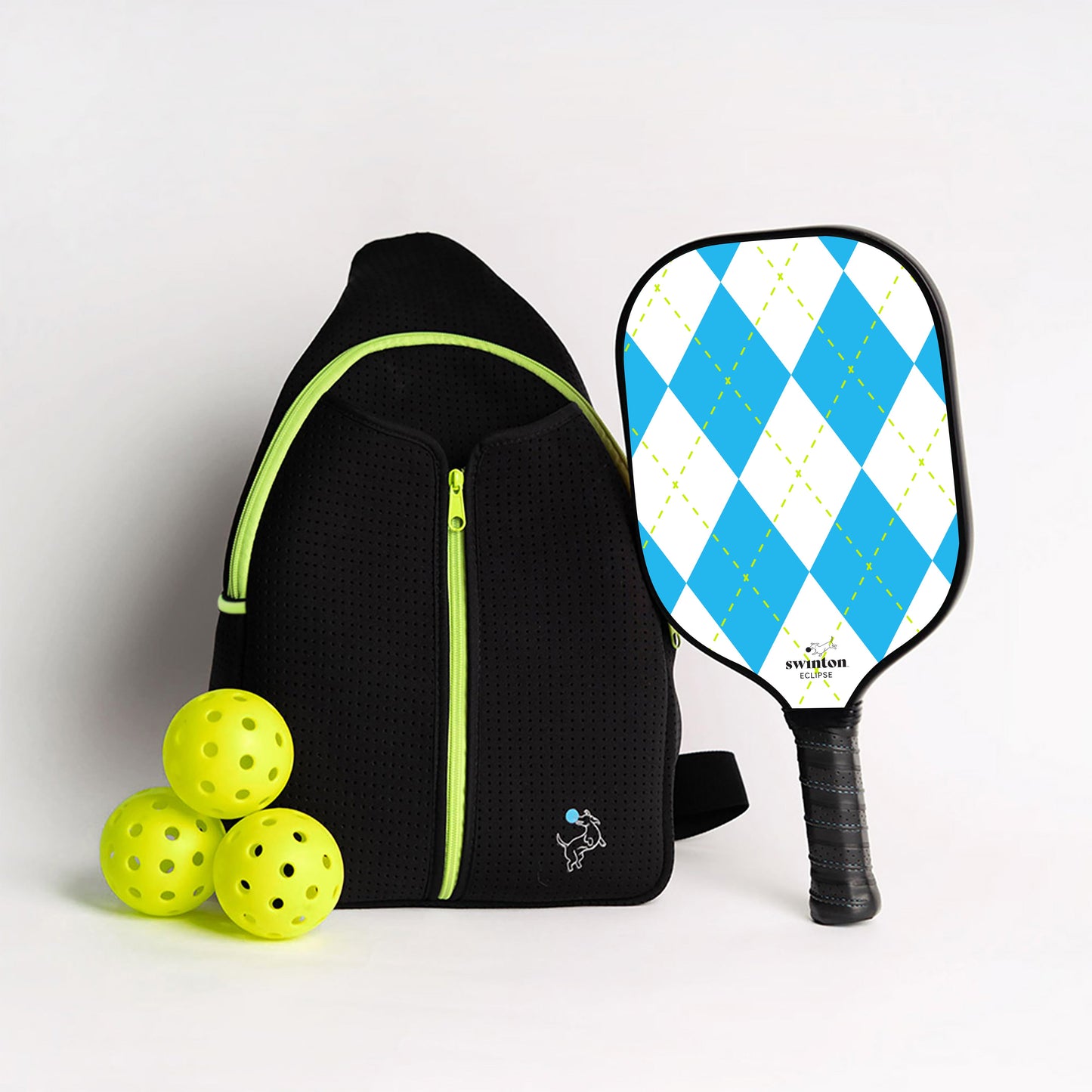 The Swinton Pickleball Starter Bundle - Black Sling Bag Combo includes a black sports backpack with neon green accents, a blue and white argyle paddle, and three yellow pickleballs—perfect as pickleball gifts or essential accessories.