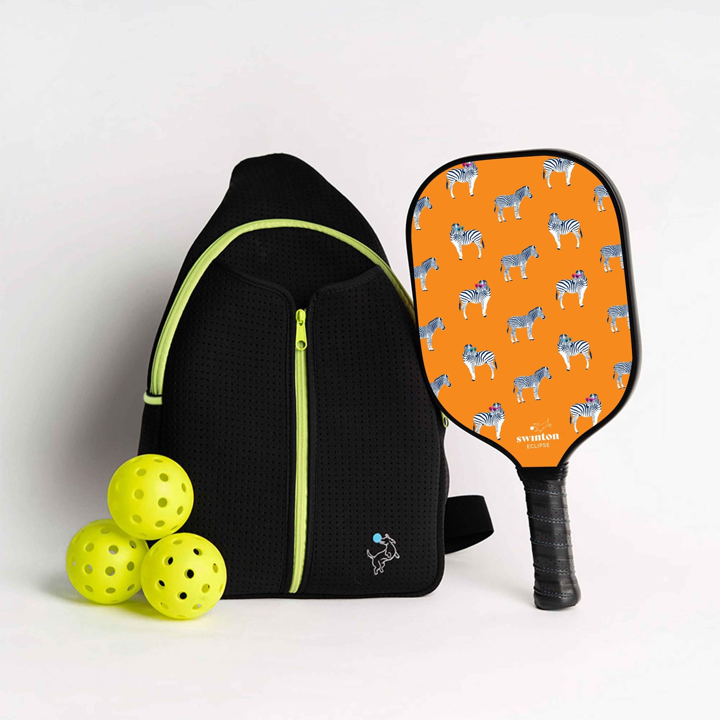 The Swinton Pickleball Starter Bundle - Black Sling Bag Combo features a sleek black bag, three yellow pickleballs, and a vibrant paddle with an orange face and blue-gray zebra pattern—perfect as a unique gift or stylish pickleball accessory.