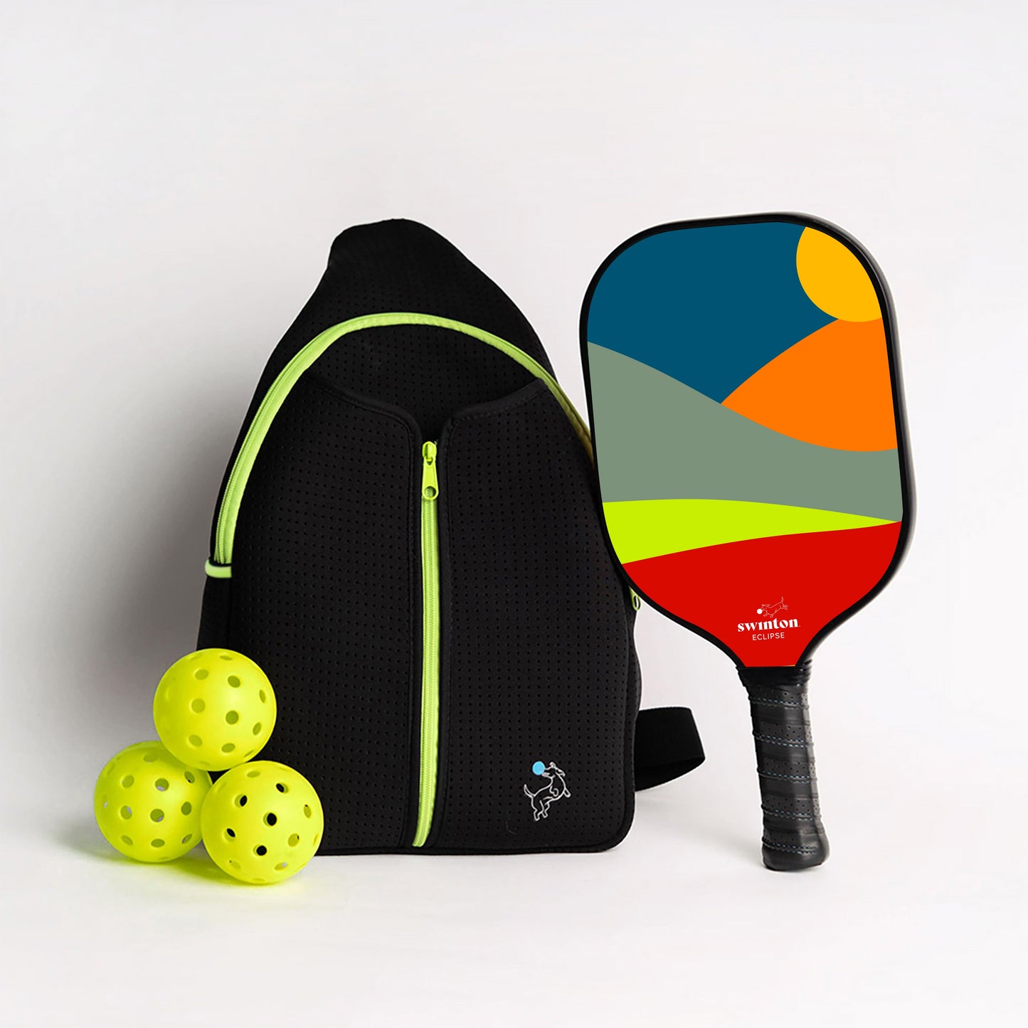The Swinton Pickleball Starter Bundle - Black Sling Bag Combo includes a black sports backpack with lime green trim, three bright yellow pickleballs, and a paddle with a bold geometric abstract landscape—an ideal pickleball gift.