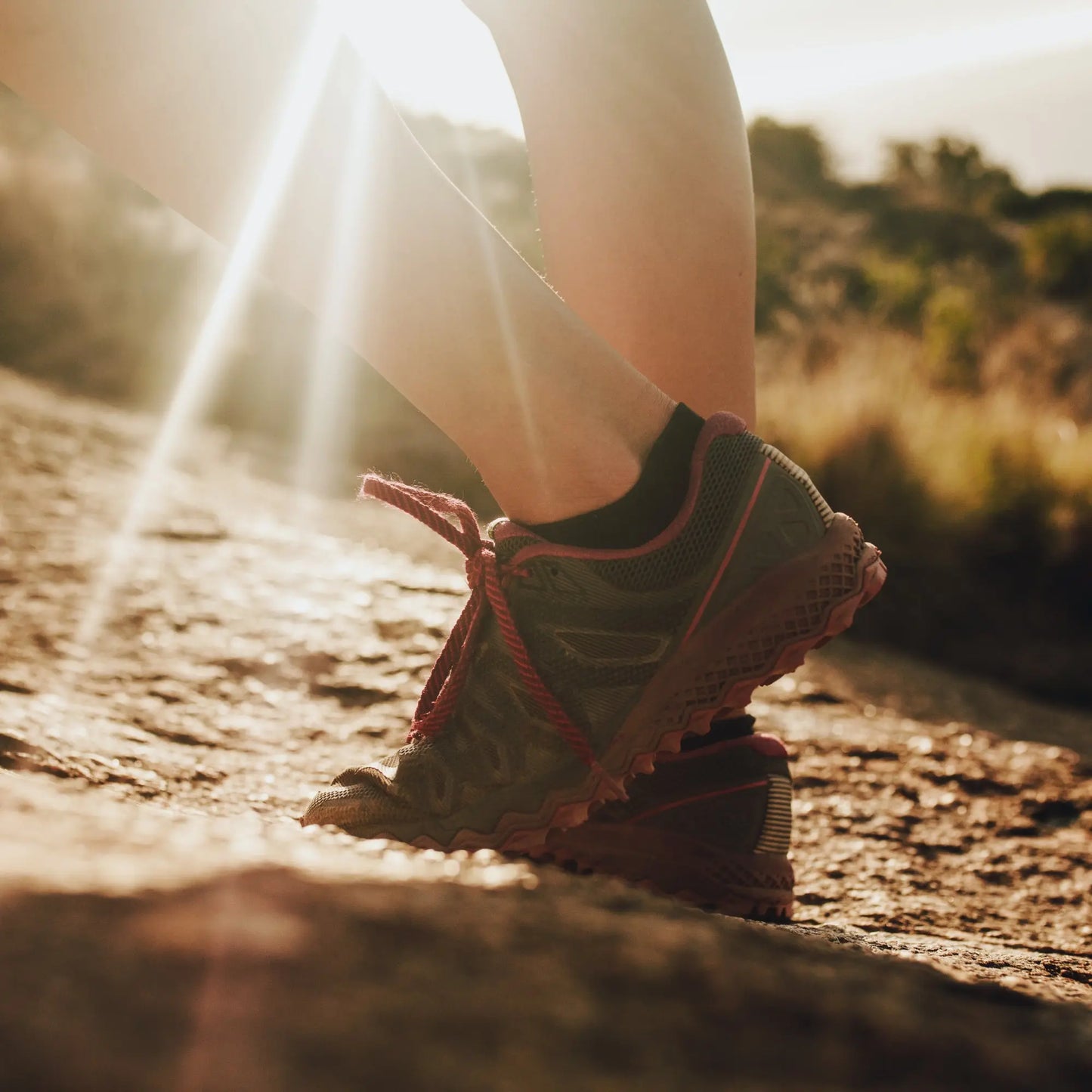 Close-up of a person’s legs in black and red athletic shoes on a sunlit trail, with greenery blurred behind—a perfect moment to trust the KT Tape KT Health Blister Treatment Patch for comfort and blister healing.