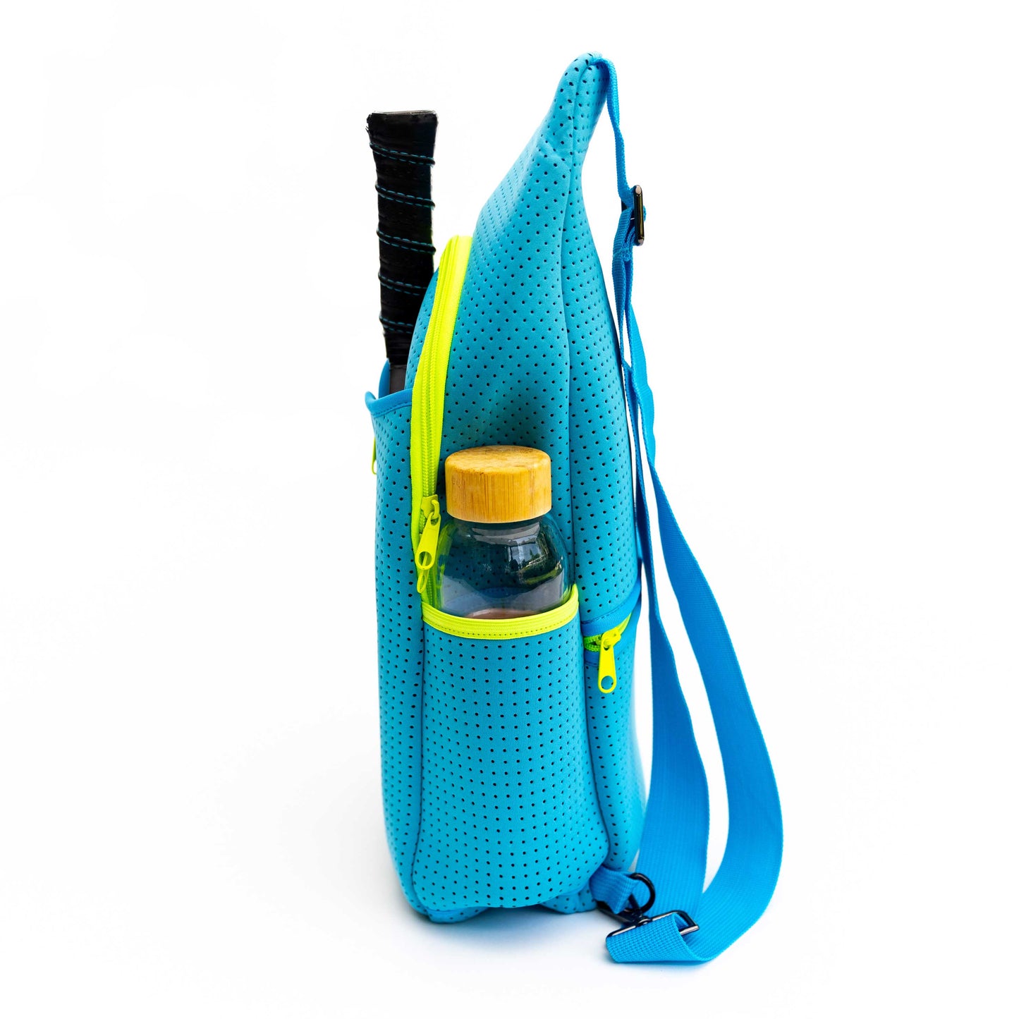 The Swinton Pickleball Sling Bag in bright blue neoprene stands upright with a yellow zipper, showing a racket handle and a bamboo-lid bottle inside. An adjustable blue strap completes this sporty bag's look against a white background.