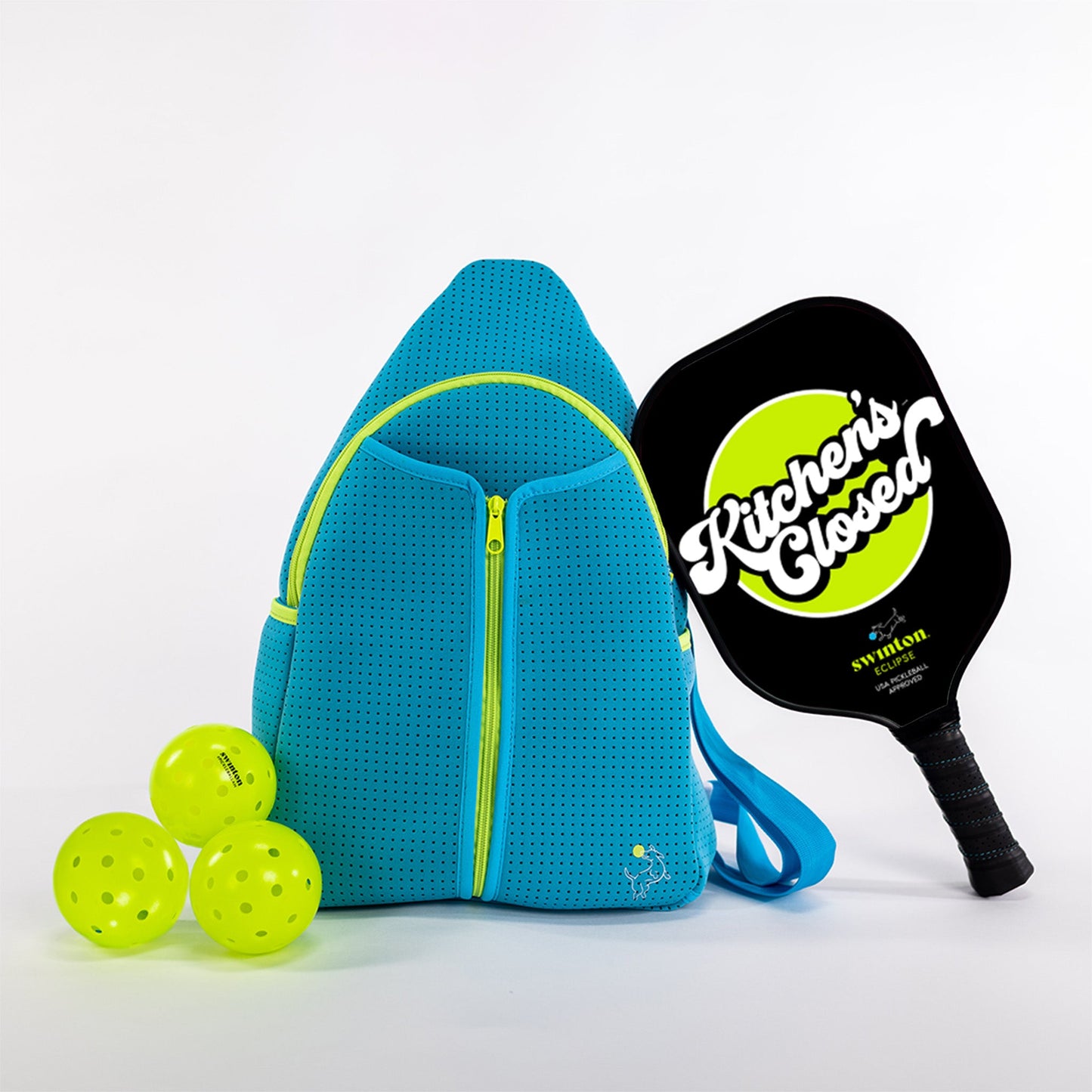 The Swinton Pickleball Starter Bundle - Blue includes a blue backpack with yellow zippers, three yellow pickleballs, and a black paddle marked “Kitchens Closed”—a perfect pickleball gift or starter set, pictured on a white background.