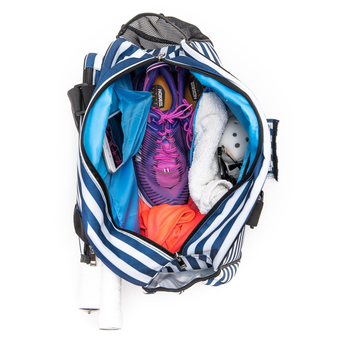 The Pik'le'Ball Sports Stylish Stripe Premium Women's Pickleball Bag, shown open, reveals purple athletic shoes, a rolled white towel, a white perforated water bottle, and an orange garment inside. Two racket handles stick out from the side pocket.
