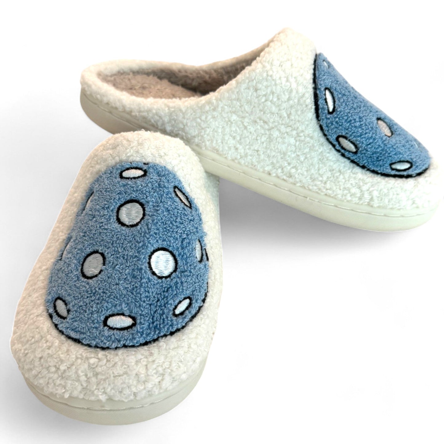 Pickleball Slippers by Fresh Pickle: cozy off-white slippers with a fluffy texture, closed-toe and open-heel. Each features a blue oval patch with white polka dots. The slippers are shown crossed on a white background.