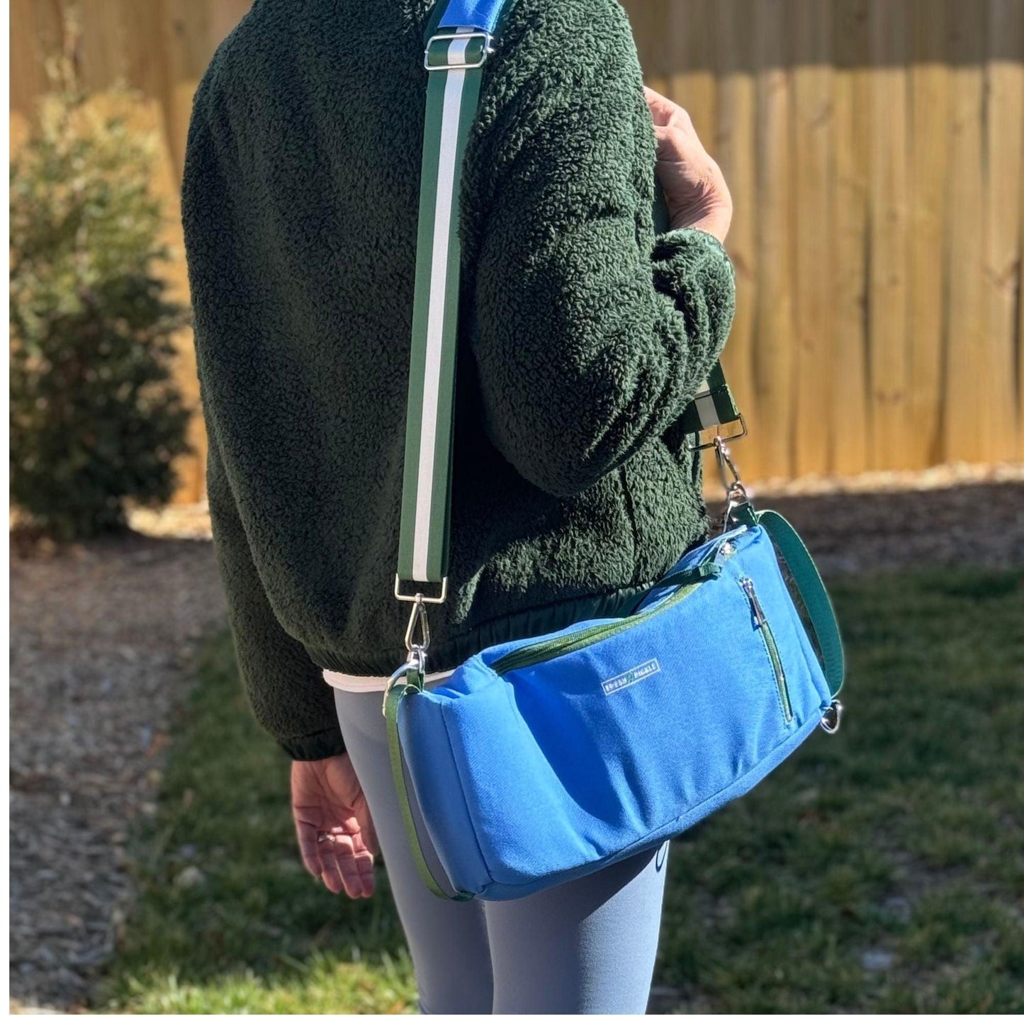 A person with a green jacket and blue bag carries their court essentials in the stylish Fresh Pickle Insulated Cooler Bag.