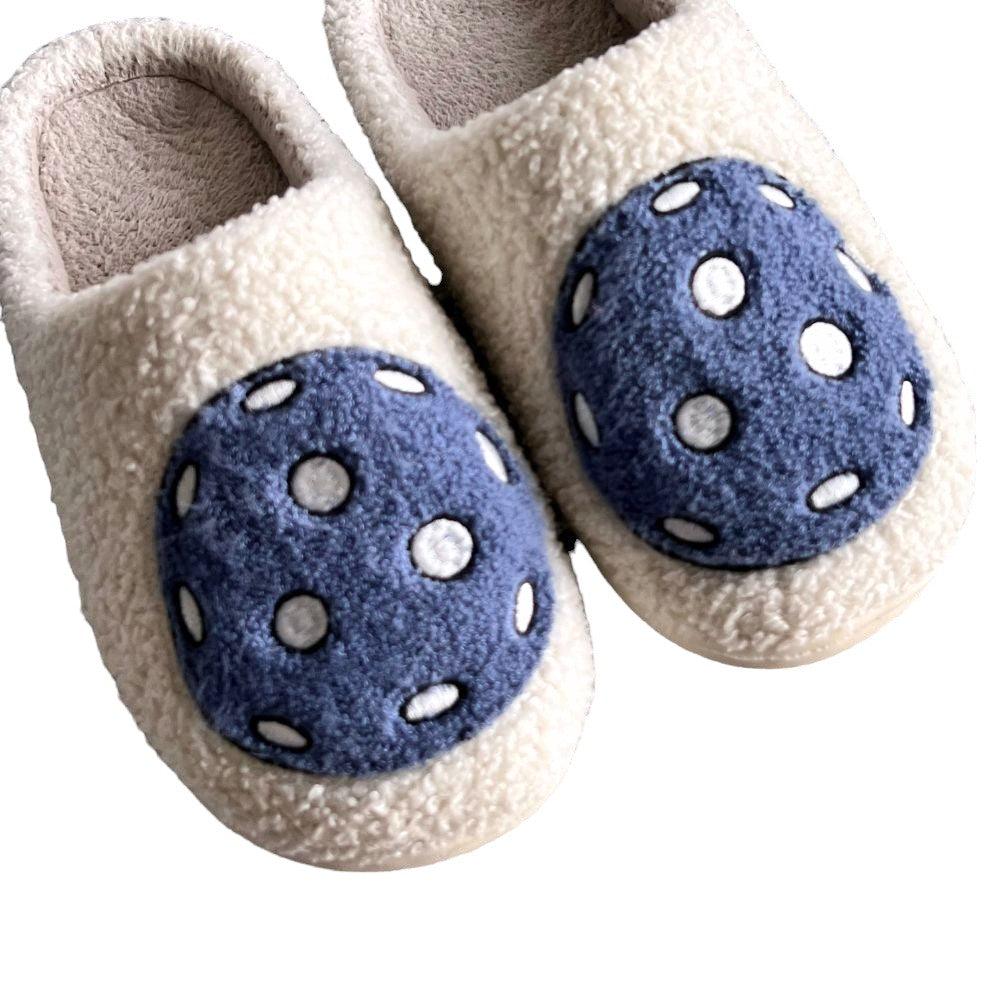 Fresh Pickle’s Pickleball Slippers are cream-colored and fluffy, made with soft, textured fabric. Each features a large round blue patch with six white dots for a fun, playful polka-dot look.