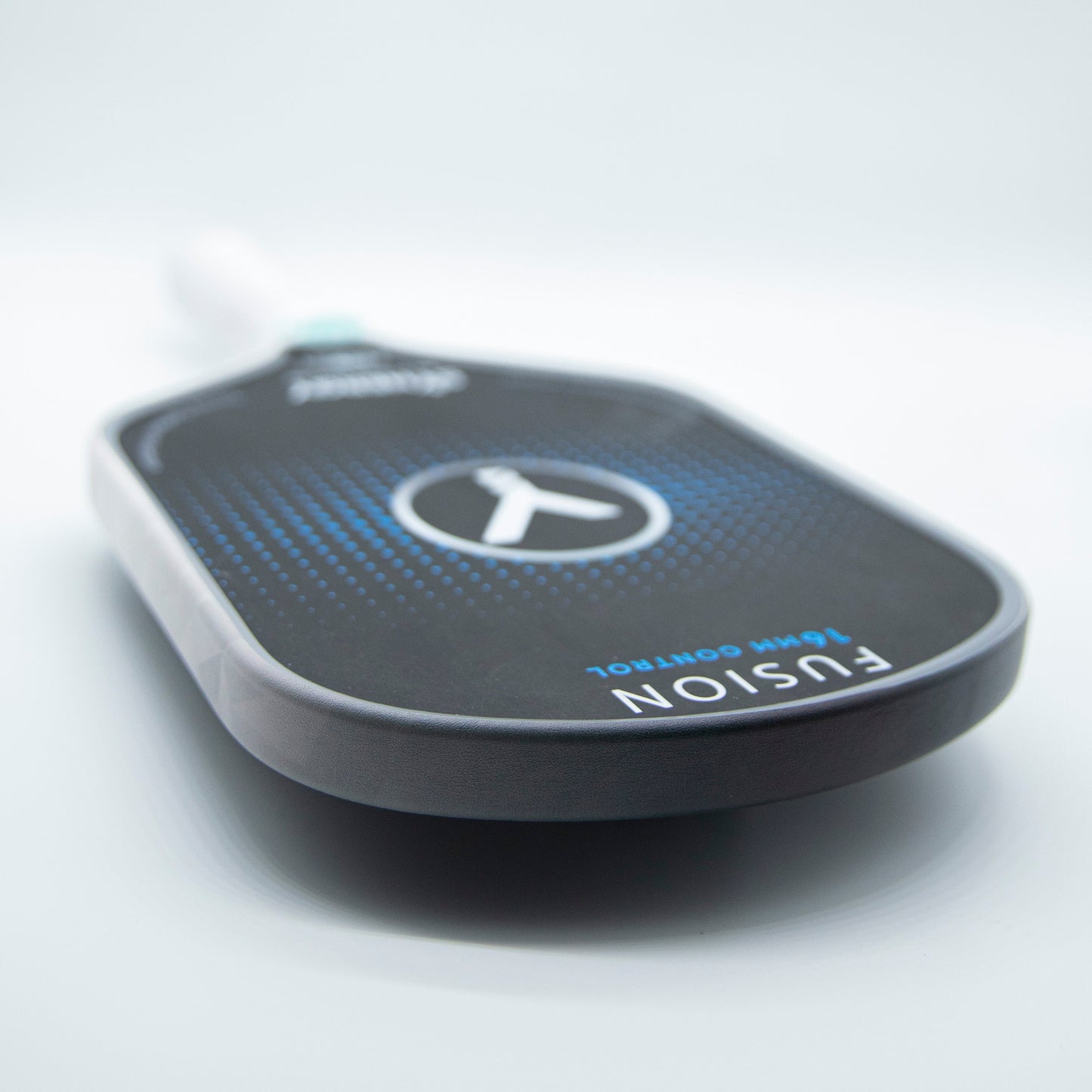 Close-up of a black pickleball paddle with blue gradient dots and a large white X. Bodhi Performance - Premium Edge Tape for Professional Edge Guard Protection shields the edge, with "FUSION" and "16mm CONTROL" printed on it. Plain light gray background.