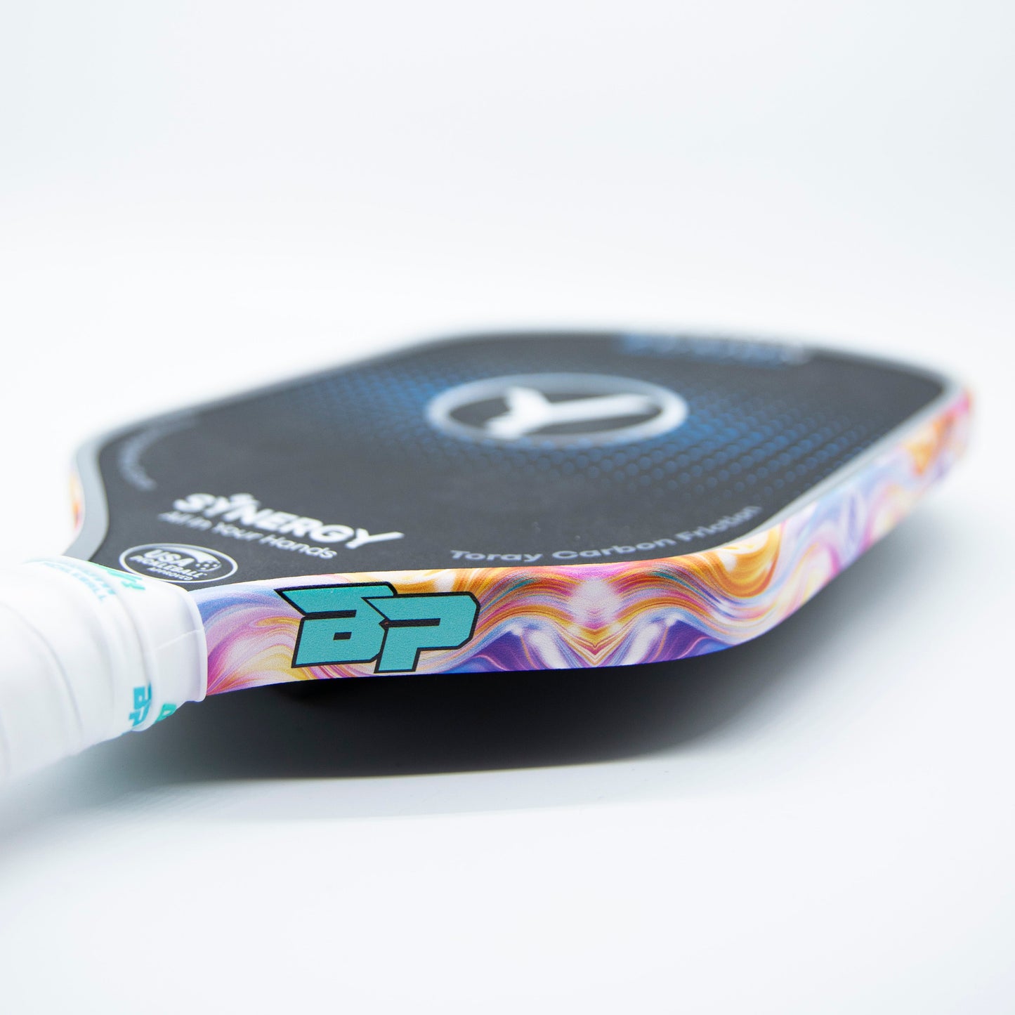 Close-up of a black pickleball paddle featuring Bodhi Performance - Premium Edge Tape for professional edge guard protection, with a colorful swirl edge, white grip, and blue-green “BP” logo standing out on a plain background.