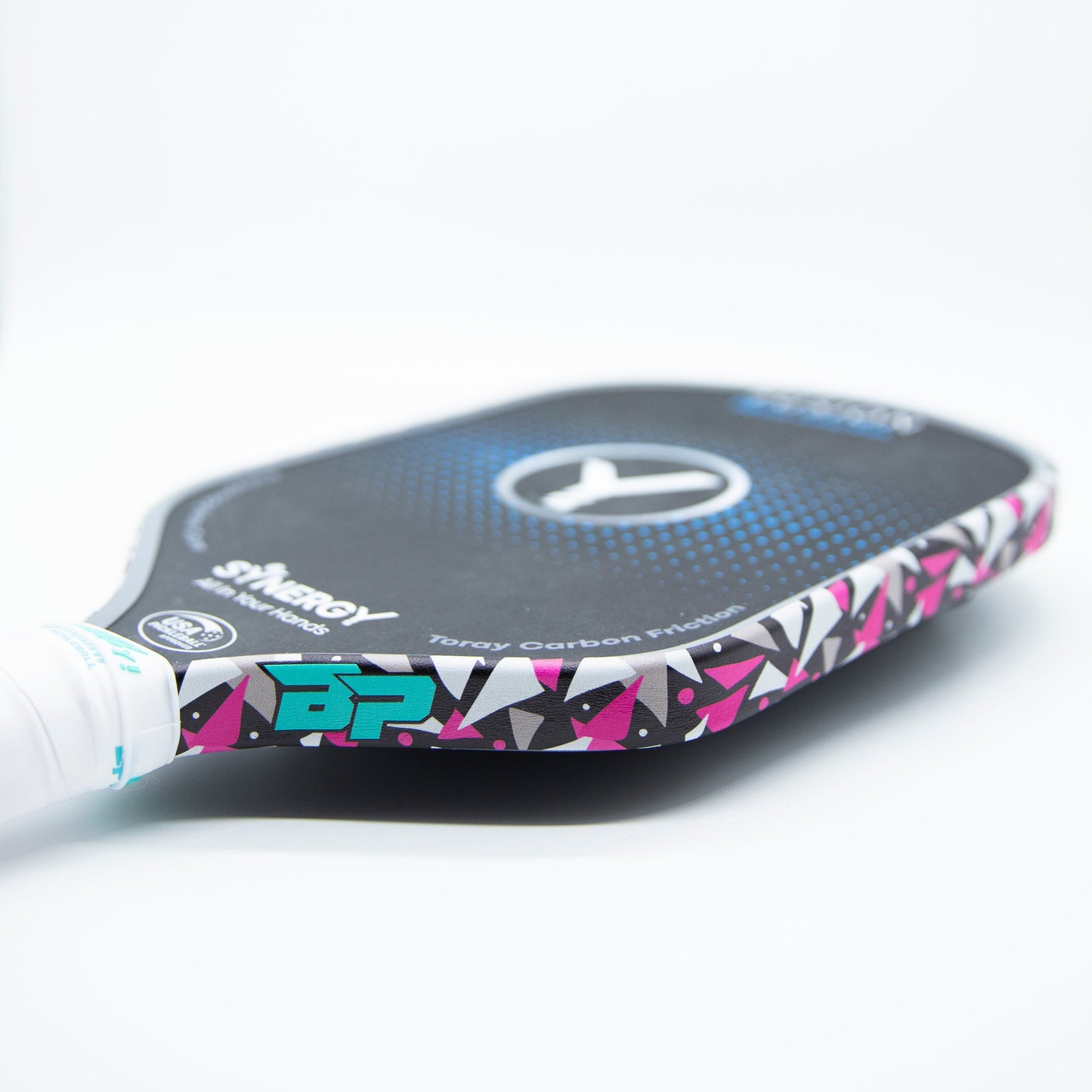 Close-up of a Bodhi Performance pickleball paddle with black face, blue and white logo, and pink/white/black geometric edge featuring Bodhi Performance - Premium Edge Tape for professional protection. Handle wrapped in white grip tape; Synergy & Targa Carbon Fiber visible.