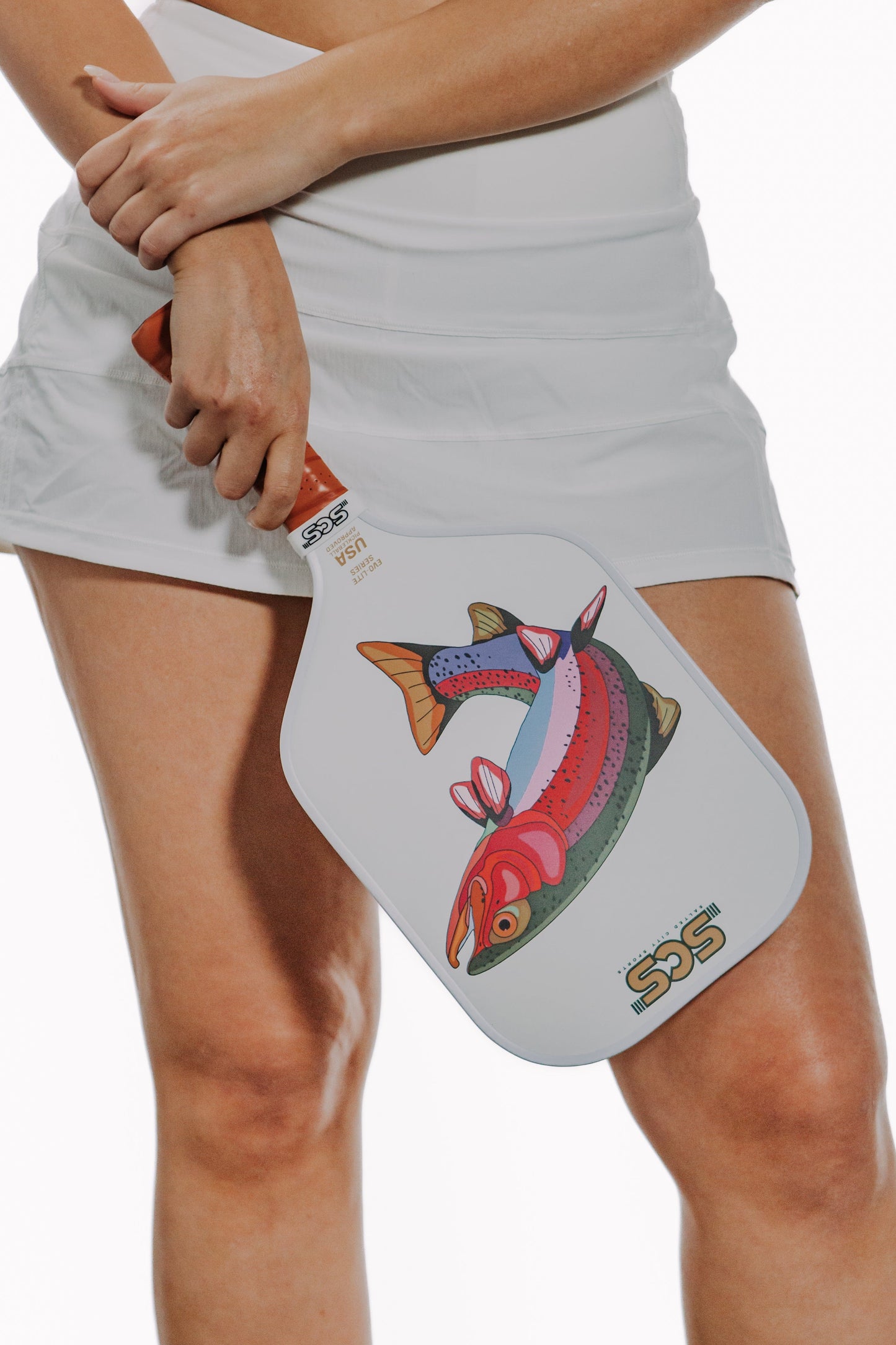 A person in a white skirt holds the Salted City Sports Bow | Evo-Lite Series pickleball paddle, featuring a colorful fish design. The USA Pickleball approved paddle is shown against a white background, image cropped at waist and knees.