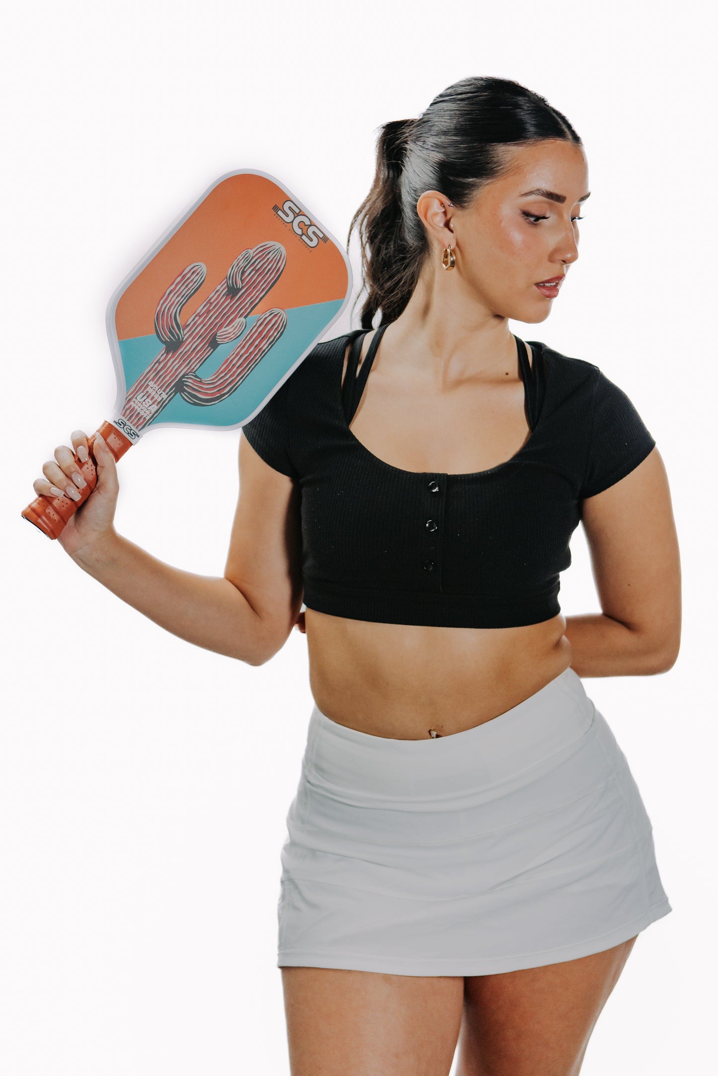 A woman in a black crop top and light gray athletic skirt holds the Cacti | Evo-Lite Series pickleball paddle by Salted City Sports. Featuring a cactus design, this USA Pickleball-approved paddle is shown against a white background.
