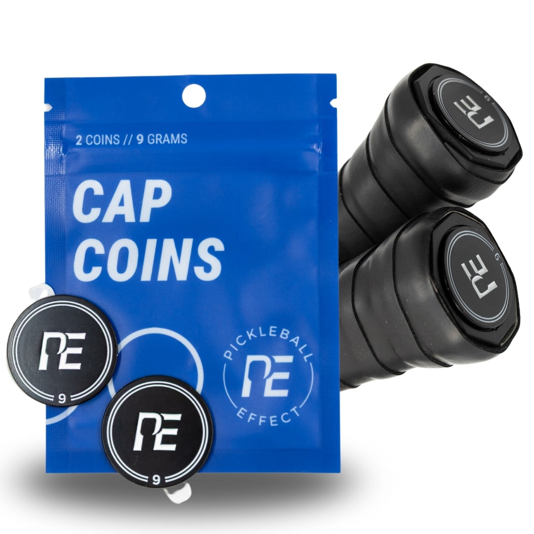 A blue Cap Coins pouch from Pickleball Effect Shop holds two black coins for paddle balance customization. Two black paddle grips with "PE" logo end caps are also shown beside the pouch.