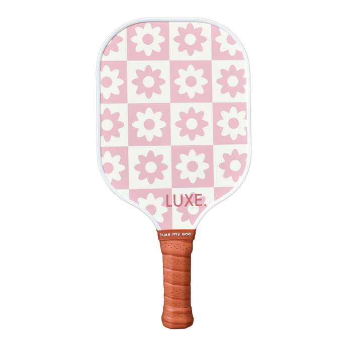 The LUXE Pickleball Checkered Flower paddle is USA Pickleball Approved, featuring a brown leather grip and a pink-and-white checkerboard face with flower accents. "LUXE." is printed in pink for elevated pickleball performance.