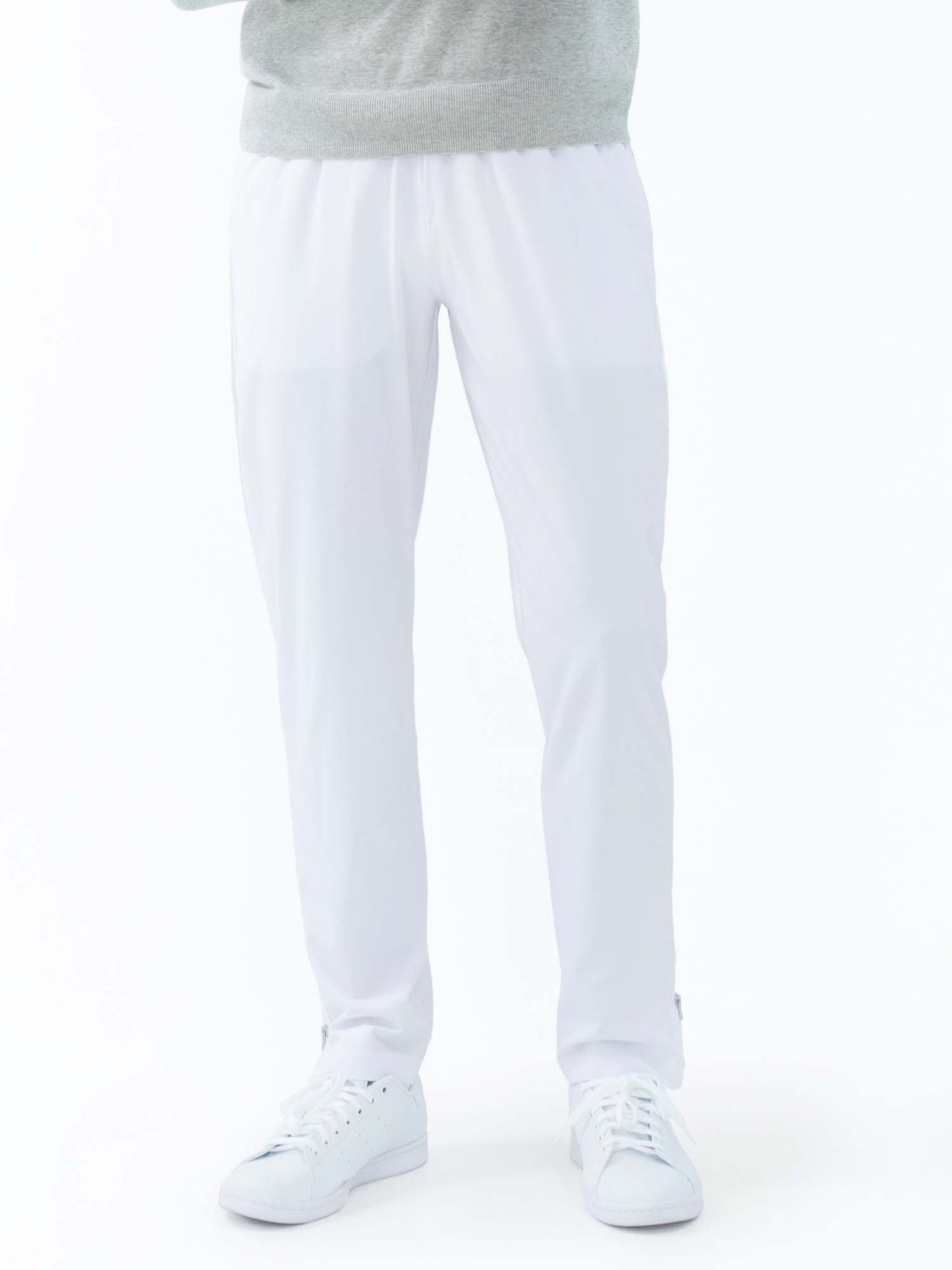 A person wears inPhorm NYC Classic Performance Men's Tennis Pant in white, paired with white sneakers and a light gray sweatshirt. Only the lower body is visible against a plain white background, creating a clean, casual look.