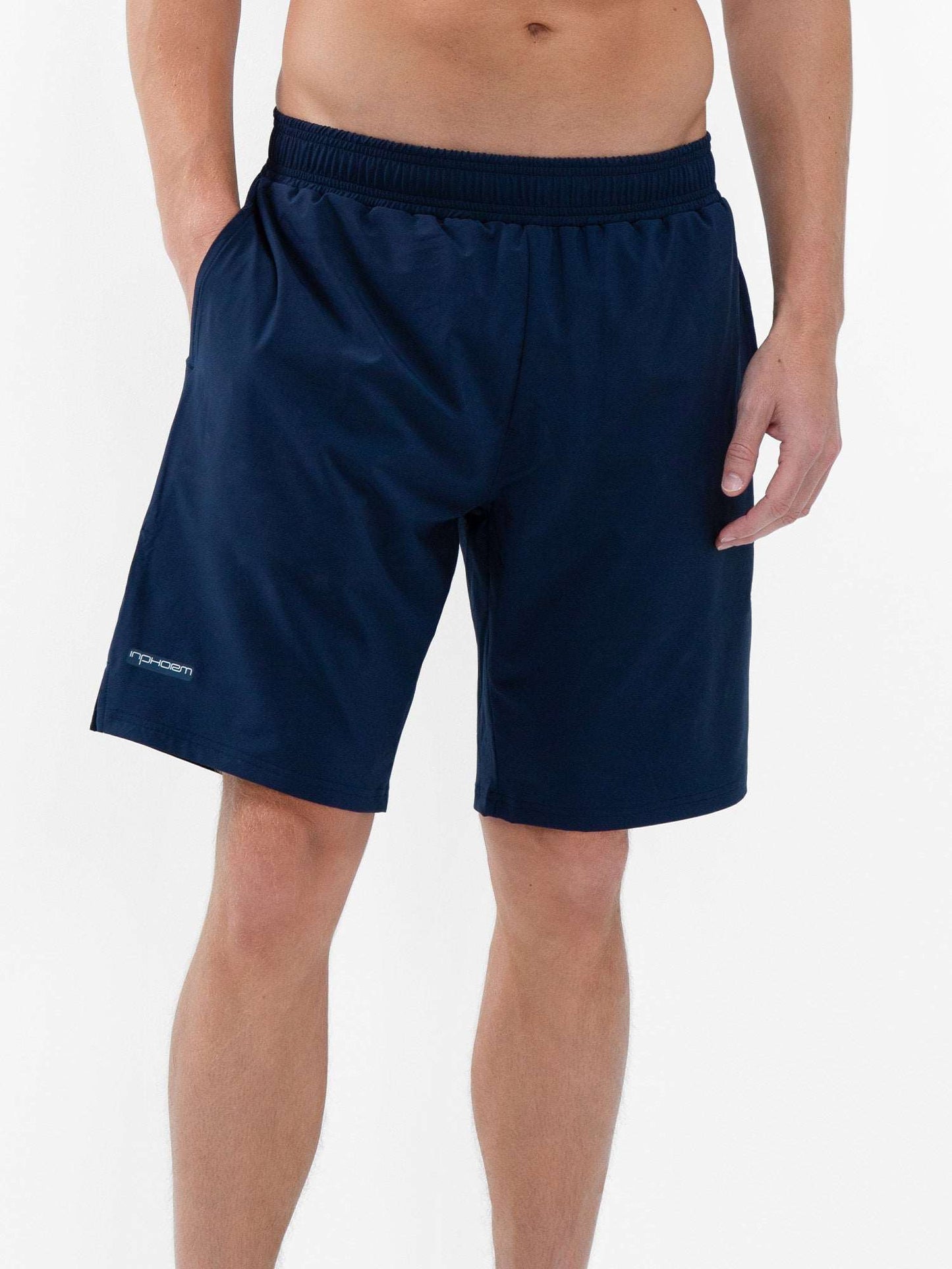A person models the inPhorm NYC Classic Performance Men's Tennis Short in Midnight, featuring a stretch woven fabric, elastic waistband, quick-dry material, and a small logo on the left leg against a plain white background. Only the lower body is shown.