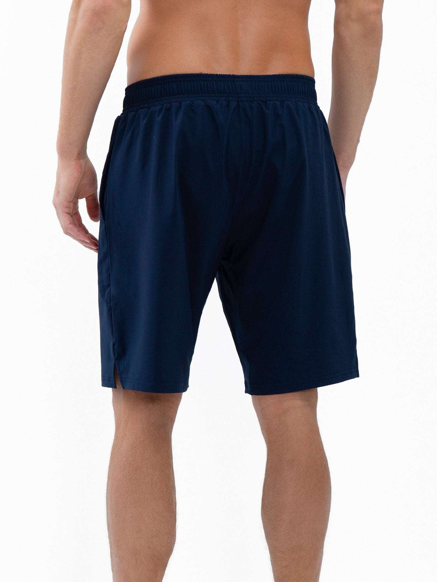 A man is seen from behind, shirtless, wearing inPhorm NYC Classic Performance Men's Tennis Short in Midnight, featuring a stretch woven lightweight fabric, elastic waistband, and quick-dry knee-length design against a plain white background.