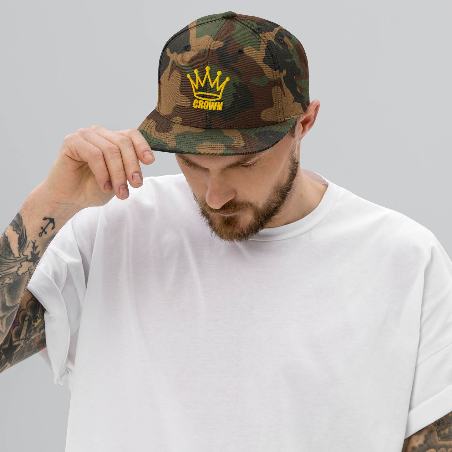 A man with tattoos on his arm wearing a Crown Pickleball - Corona Snap-back Hat (Camo) by Crown Pickleball.