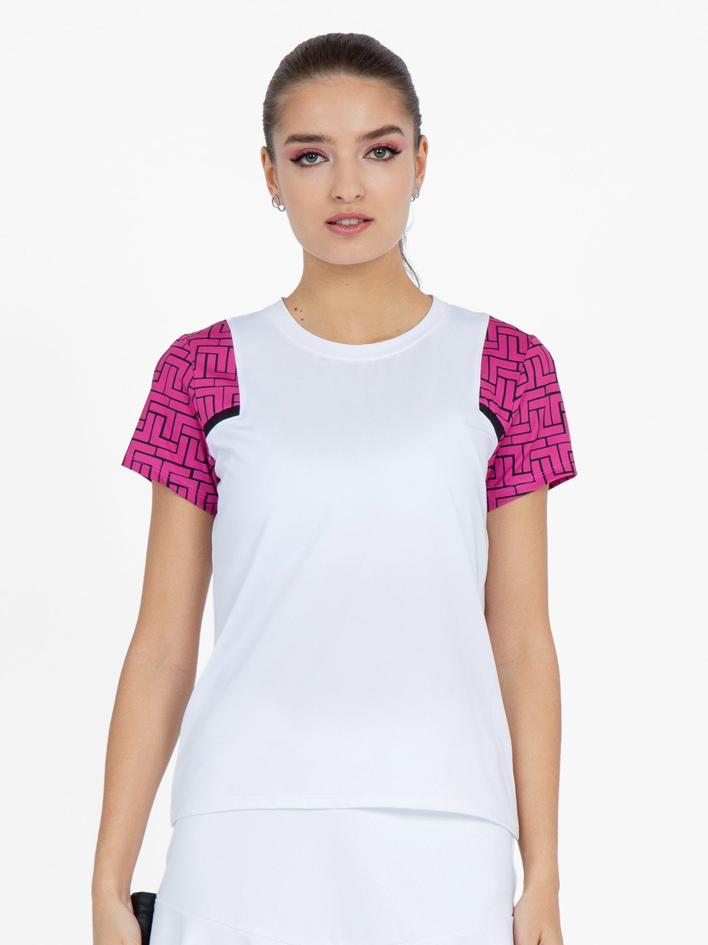 A woman faces forward against a white background, wearing the inPhorm NYC Colorblock Active Sofia Short Sleeve Crew Neck in Raspberry Pink, featuring bright patterned sleeves. Her hair is tied back and her makeup is subtle with a touch of pink eyeshadow.