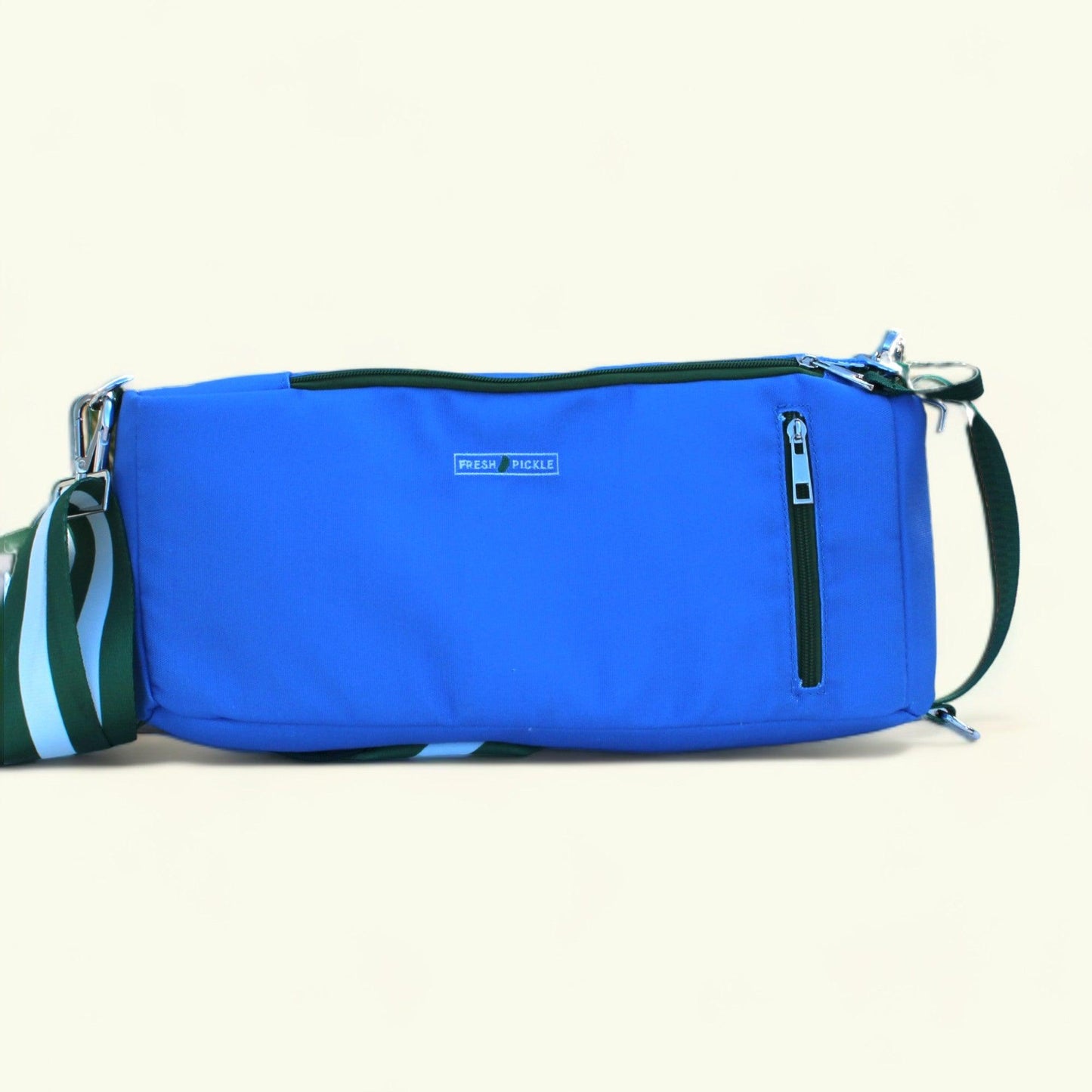 The Fresh Pickle Insulated Cooler Bag is bright blue and rectangular, featuring a zippered front pocket, an adjustable green strap with light blue and white stripes, and a small “PICKLE PICKLE” label—perfect for carrying court essentials.