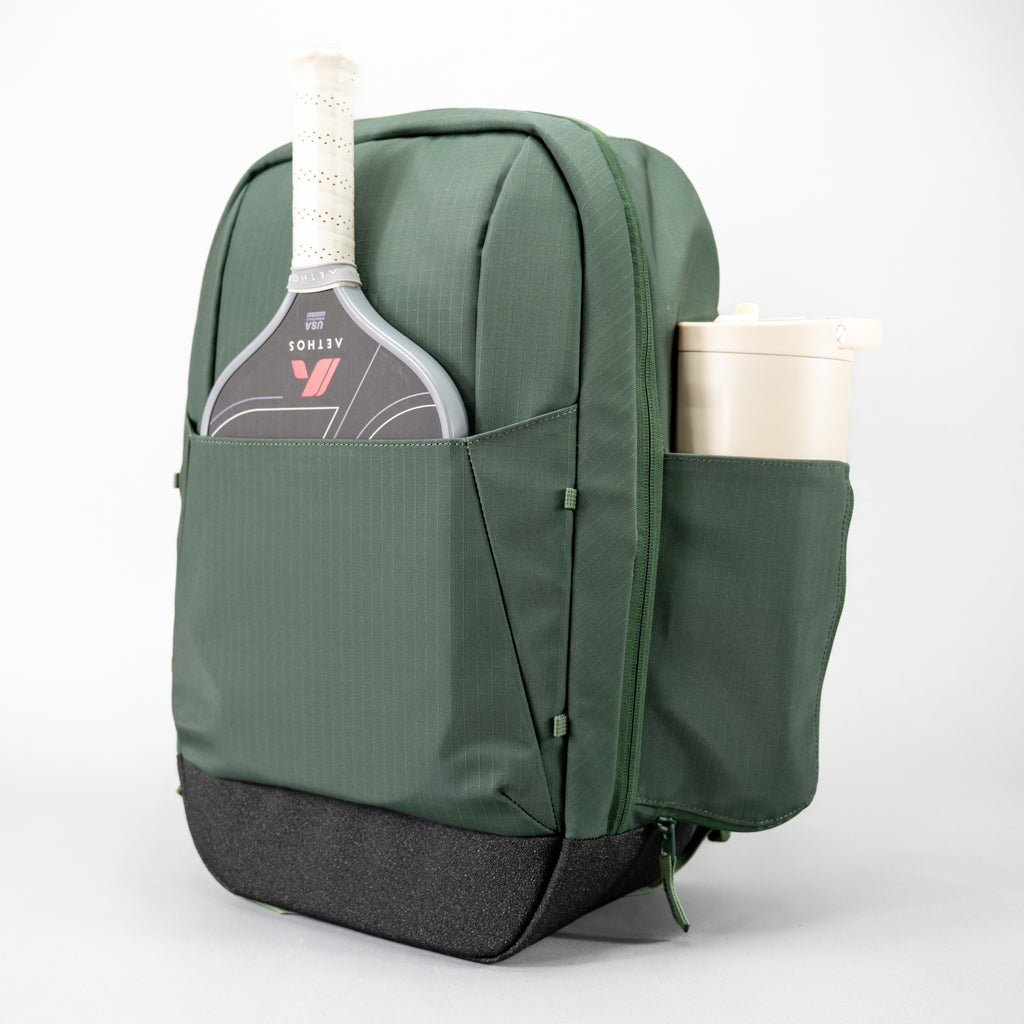 The FORWRD Court Ranger Pickleball Backpack in dark green features a front pocket for your paddle, a side pocket for a beige water bottle, and a textured black base. Its structured design and practical features make it one of the top pickleball bag choices. White background.