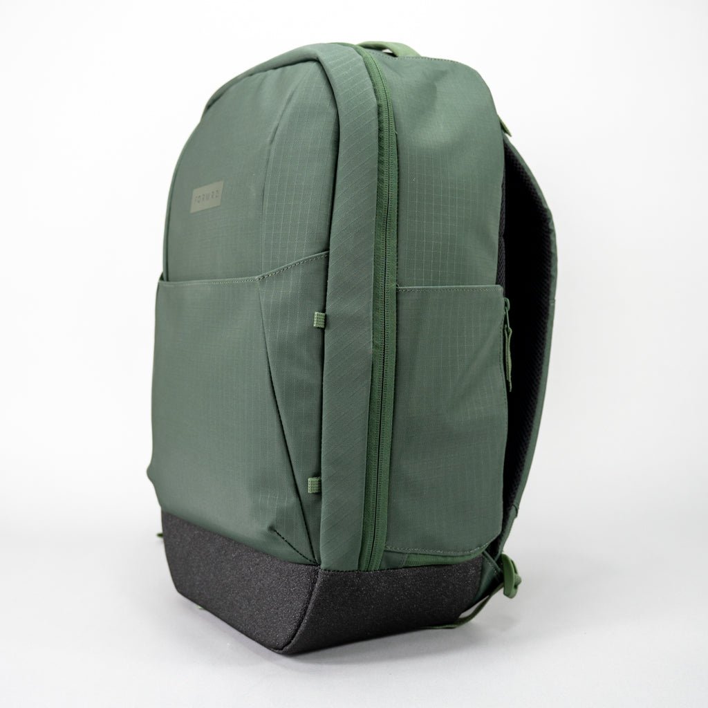 The FORWRD Court Ranger Pickleball Backpack is a sleek green bag with a minimalist design, smooth structured body, textured base, front zip pocket, and side pocket. It stands upright on a plain white background.