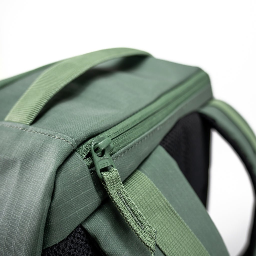 Close-up of the FORWRD Court Ranger Pickleball Backpack shows its durable green fabric, sturdy top handle, matching green zipper pull tab, and part of the shoulder strap, all set against a plain white background.