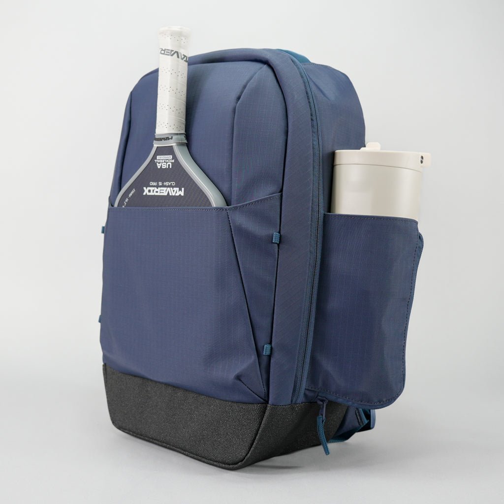 The FORWRD Court Ranger Pickleball Backpack, featuring a blue design with a black base, holds a paddle in the front pocket and a large tumbler in the side pocket. Displayed on a plain white background, this stylish bag is available for under $200.