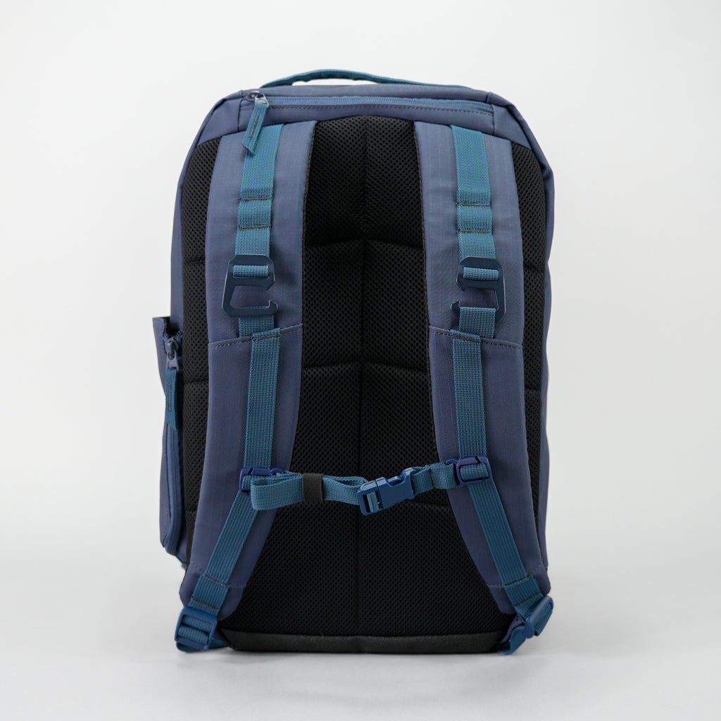The FORWRD Court Ranger Pickleball Backpack in navy blue is shown from the back, featuring padded shoulder straps, blue adjustable buckles, a chest strap, top handle, black padded back panel for comfort, and a left-side pocket.