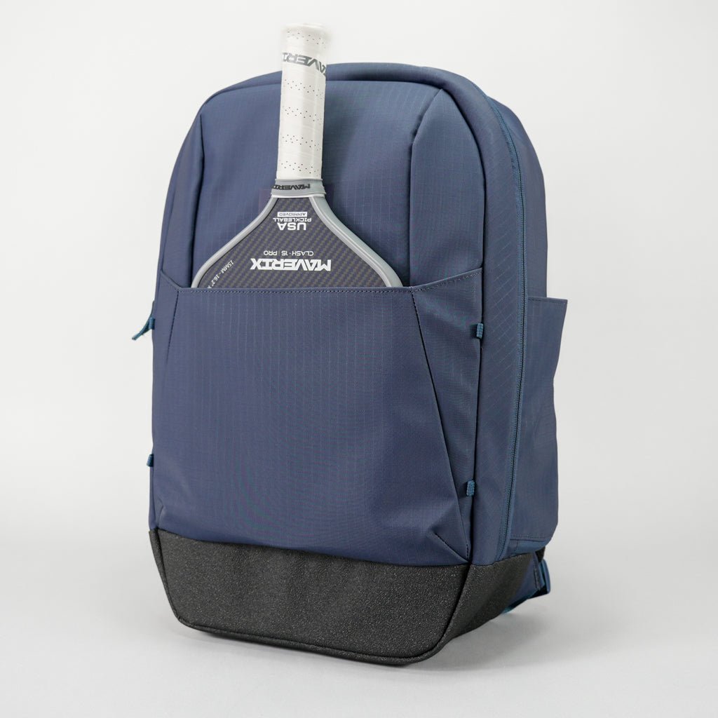 The FORWRD Court Ranger Pickleball Backpack in blue and black stands upright with a white paddle in the front pocket. Its sturdy base and modern design make it a leading pickleball bag under $200.