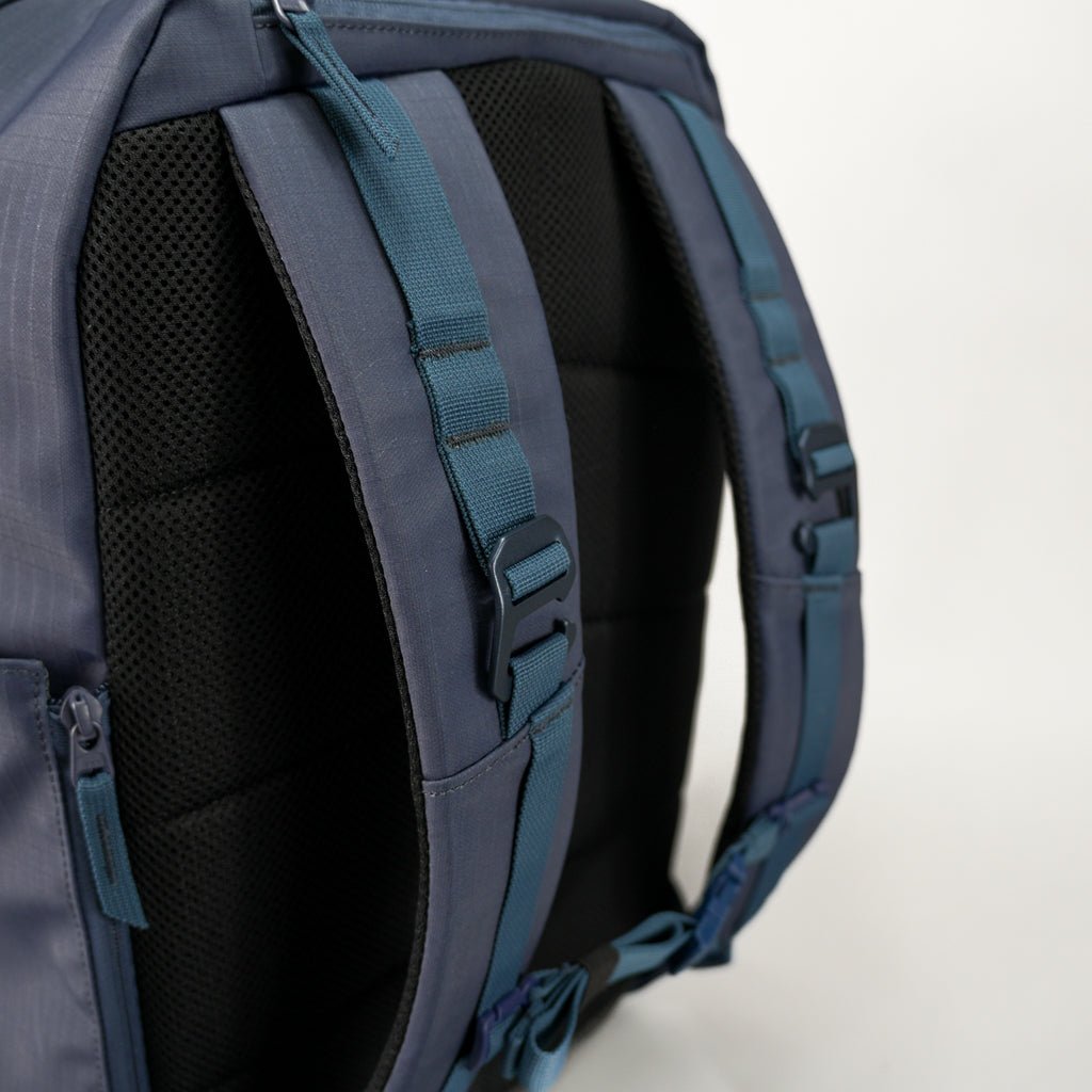 Close-up of the FORWRD Court Ranger Pickleball Backpack in dark blue, featuring padded shoulder straps with adjustable blue webbing, plastic buckles, and black mesh padding. A plain white background highlights its details and texture.