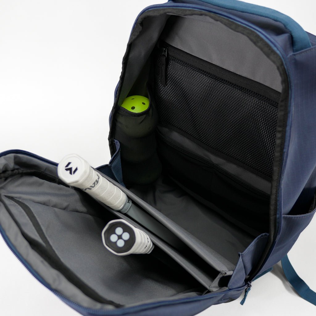 The FORWRD Court Ranger Pickleball Backpack is open, displaying two racquets with white grips, a green ball canister, and an inner mesh zip pocket all neatly arranged in the main compartment against a white background.