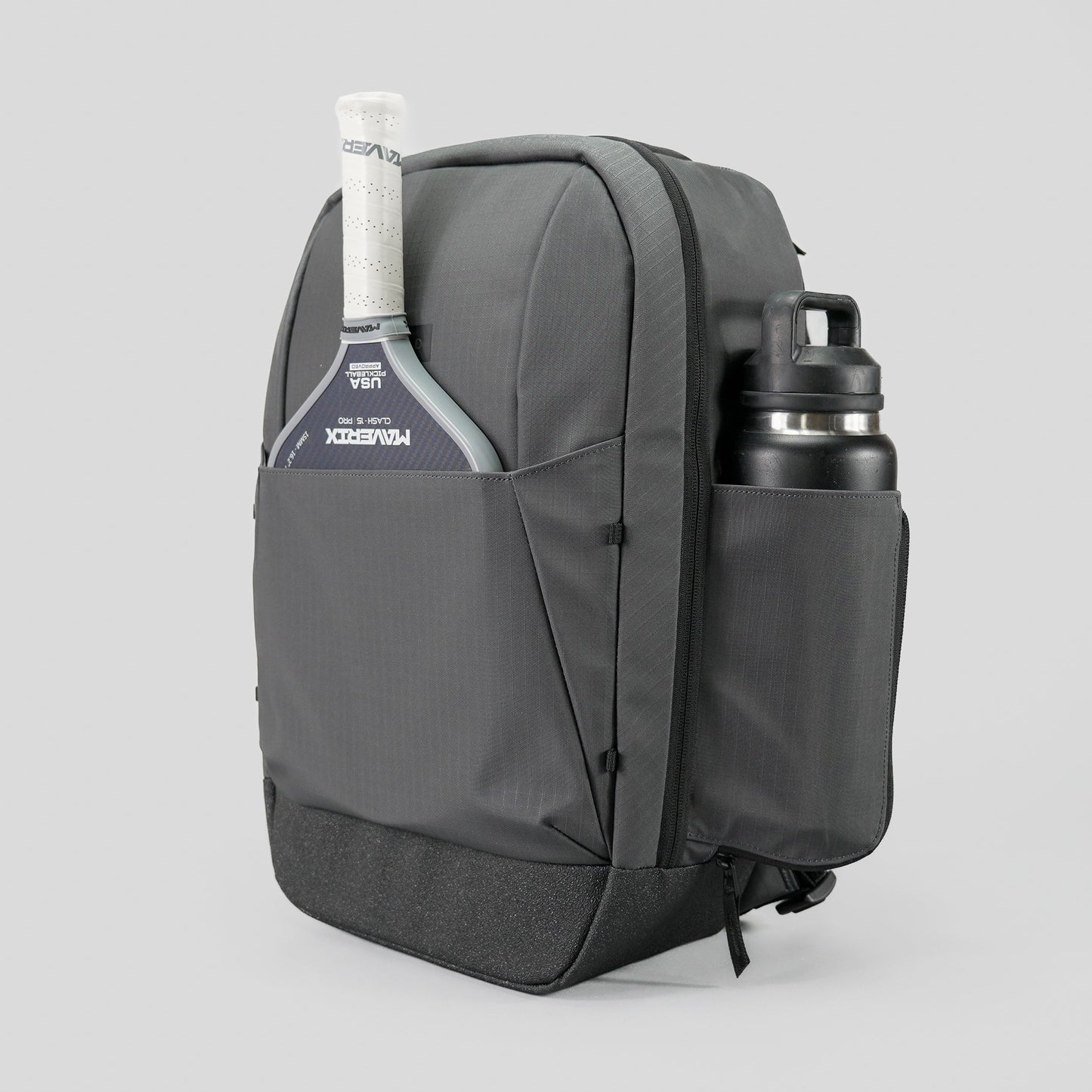 The FORWRD Court Ranger Pickleball Backpack in gray sits on a light gray background, holding a paddle with its handle out on the left and a black water bottle secured in the right side pocket for a modern, minimalist look.