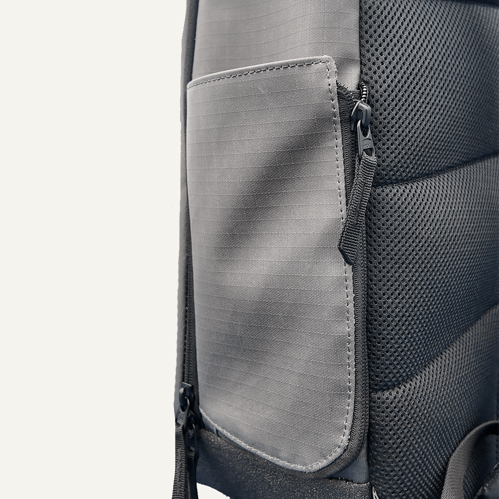 Close-up of the FORWRD Court Ranger Pickleball Backpack’s gray side pocket with a zipper. The smooth, textured fabric and padded black breathable mesh back panel enhance comfort. Shown against a plain light off-white background.