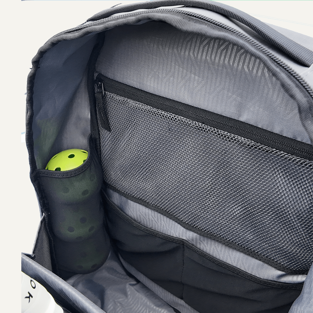 The FORWRD Court Ranger Pickleball Backpack is open, revealing a gray interior with mesh zippered and two slip pockets. A black water bottle with green cap sits in the left pocket. The lining features a subtle pattern, and the bag is empty except for the bottle.