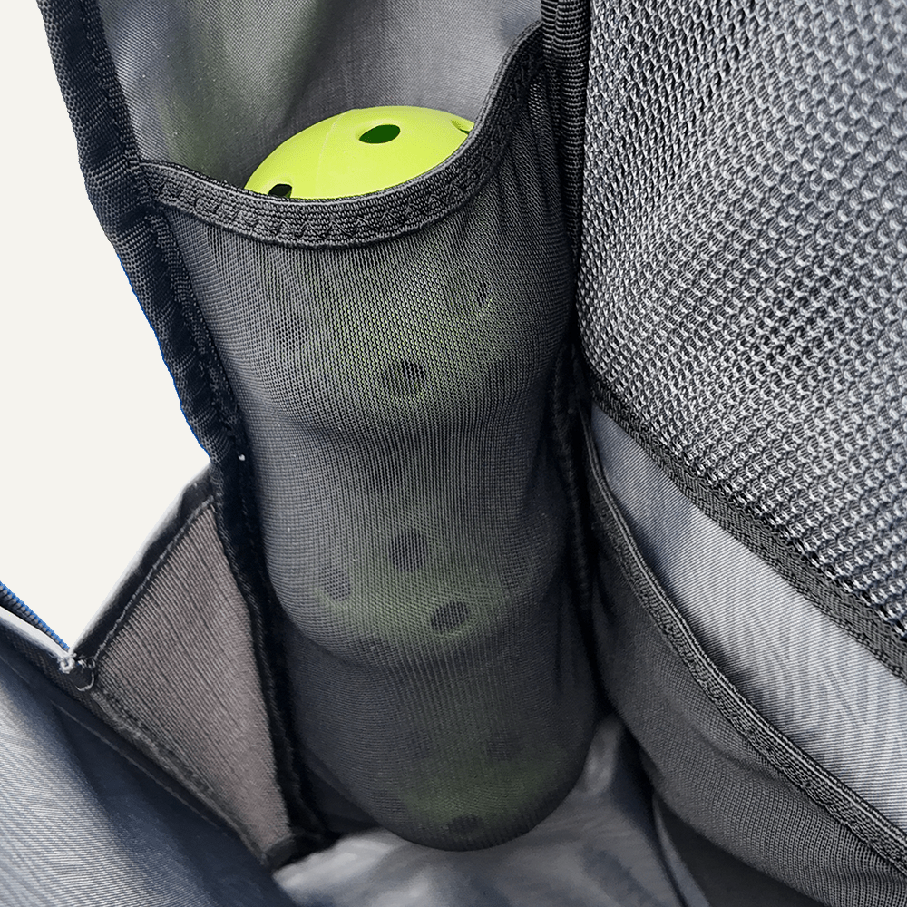 Close-up of a black mesh pocket on the FORWRD Court Ranger Pickleball Backpack holding stacked neon green balls. The interior and another zippered mesh pocket are visible. A top choice for the best pickleball bag under $200.