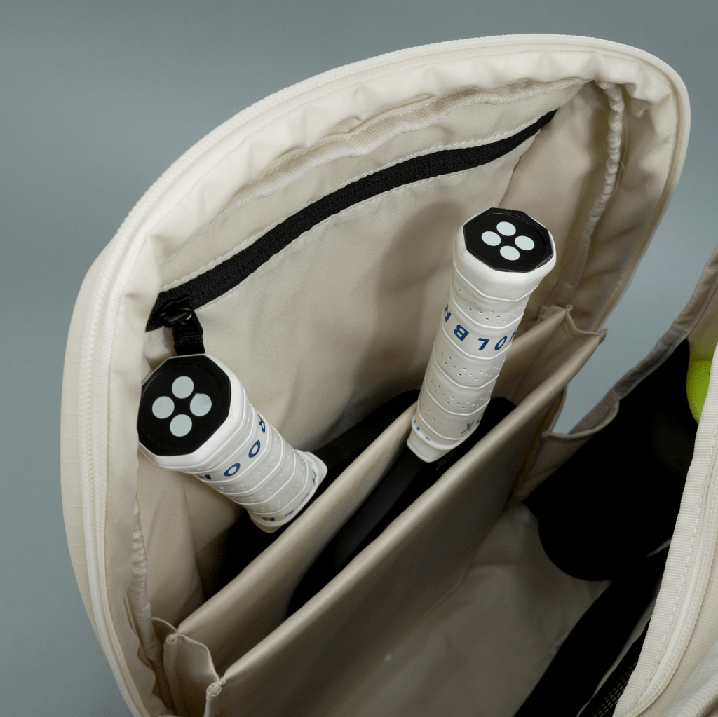 A close-up of an open FORWRD Court Ranger Pickleball Backpack reveals two rackets in a padded compartment, with an interior zipper pocket above them against a light grey background.