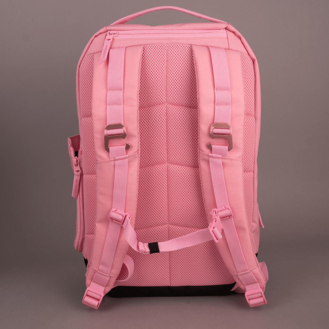 The FORWRD Court Ranger Pickleball Backpack in pink is shown upright with its back, featuring padded adjustable shoulder straps, a top handle, chest strap, mesh padding for comfort, and visible zippers and metal buckles against a gray background.