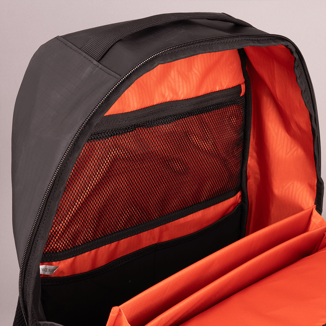 A close-up of the FORWRD Court Ranger Pickleball Backpack shows its bright orange interior, mesh zippered pocket, and padded sleeve for organizing a laptop or gear. The open black backpack sits against a neutral background.