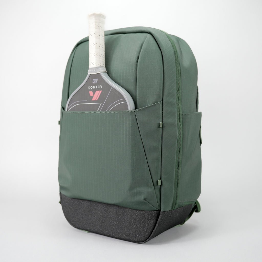 The FORWRD Court Ranger Pickleball Backpack in green with a dark gray bottom stands upright, displaying an ATOMOS 7 paddle—white grip, black face—from its front pocket. Shown on a white background, it’s perfect as the best pickleball bag under $200.