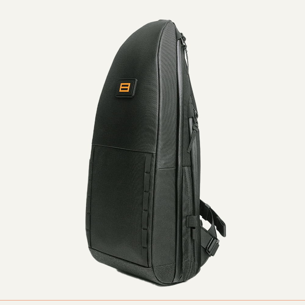 The FORWRD Cross Court Pickleball Sling is a sleek, black, teardrop-shaped bag with a small orange and black logo on the front. Lightweight and durable, it features a textured finish, side straps, and is stylishly set against a plain background.