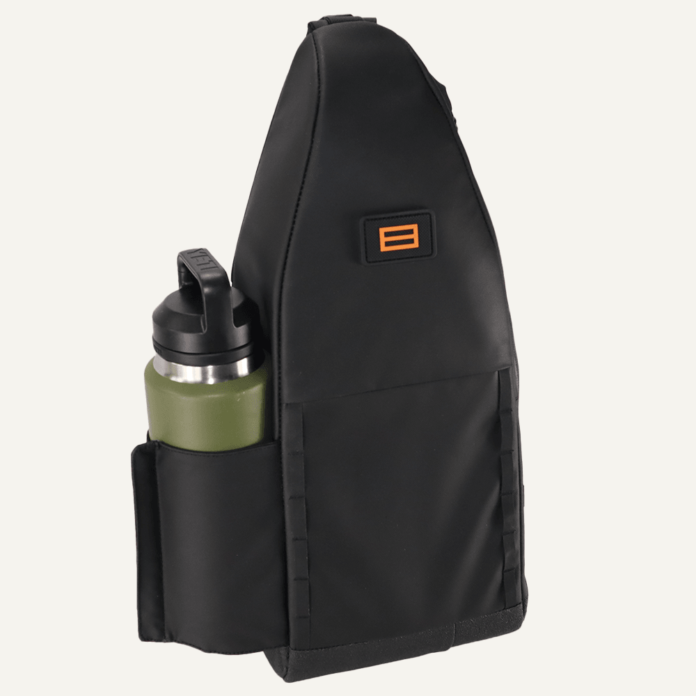 The FORWRD Cross Court Pickleball Sling is a black, triangular bag with a front pocket holding a green water bottle with a black lid. Durable and lightweight, it features an orange and black logo patch near the top, shown against a plain, light background.