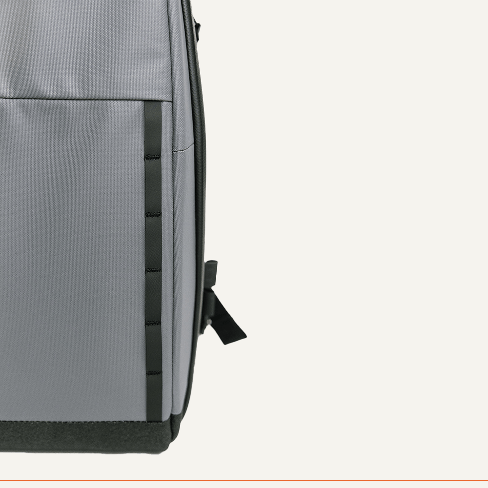 Close-up of the FORWRD Cross Court Pickleball Sling in grey fabric, featuring a vertical zipper pocket, black trim, small strap, durable darker bottom material, and a convenient paddle sleeve against an off-white background.