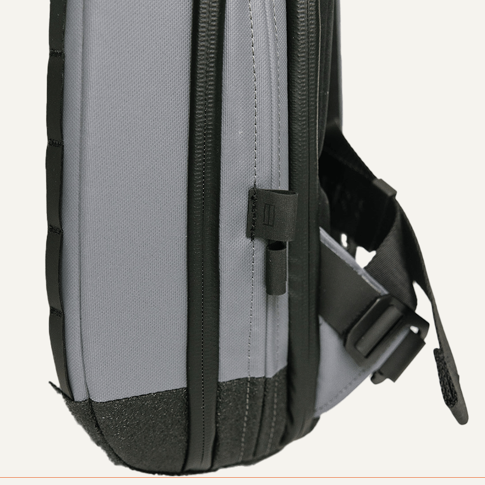 Close-up of the FORWRD Cross Court Pickleball Sling, a lightweight, durable gray and black backpack with black zippers, webbing, adjustable buckle strap, and a textured reinforced base for added support.