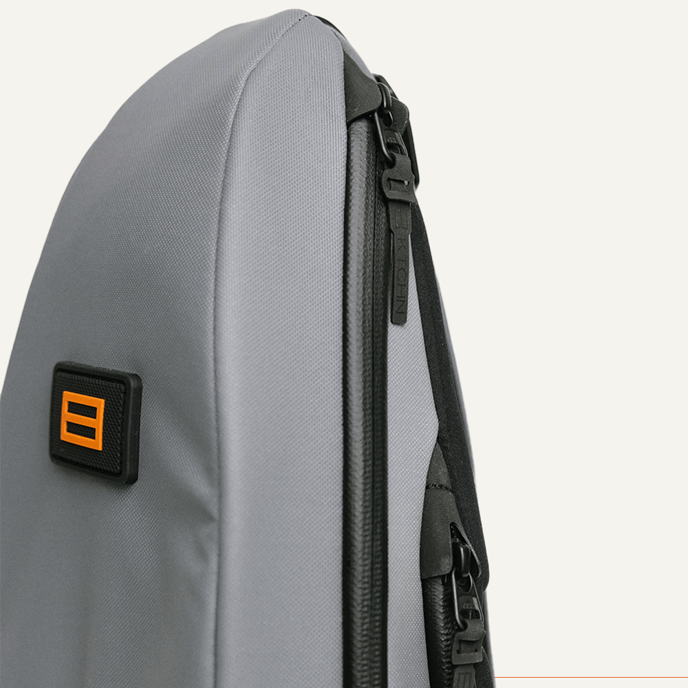 A close-up side view of the FORWRD Cross Court Pickleball Sling shows part of this sleek, lightweight, and durable backpack with black zippers and an orange-and-black FORWRD logo patch against a plain light background.
