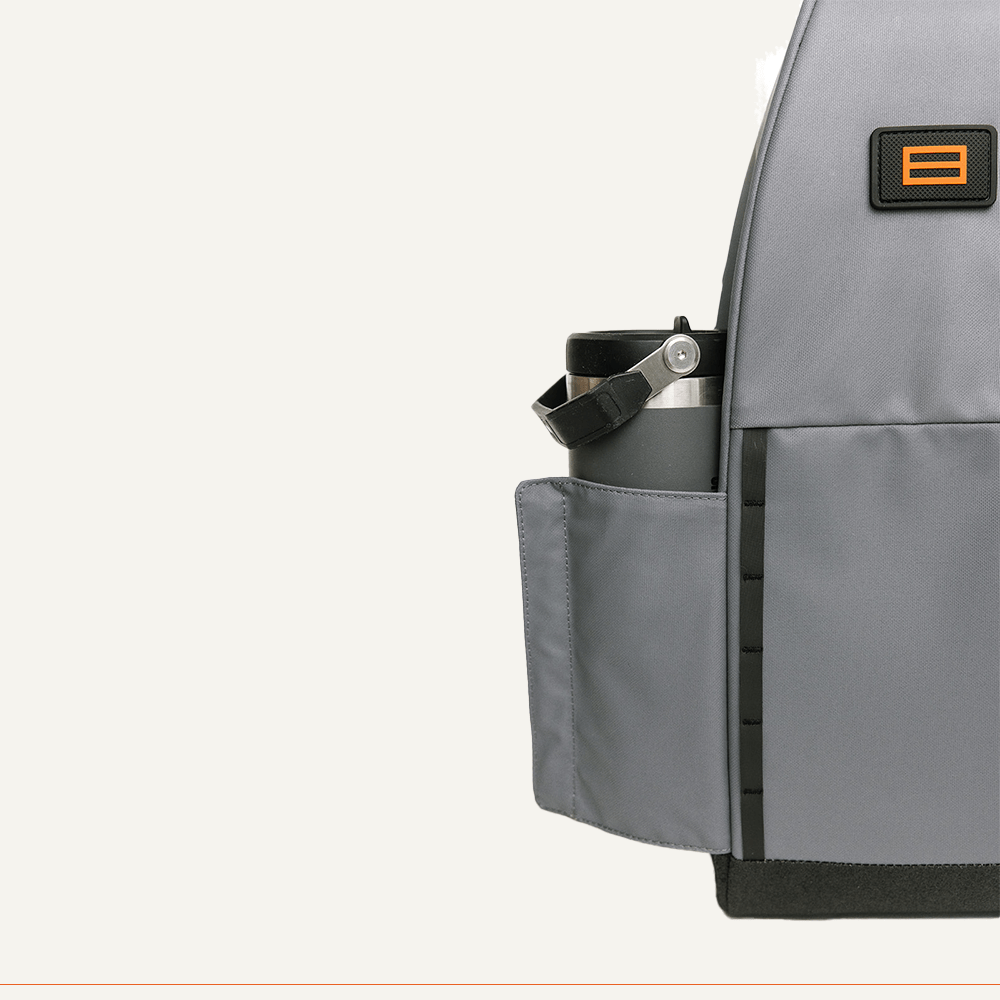 A close-up of the FORWRD Cross Court Pickleball Sling shows a side pocket holding a silver water bottle and an orange and black rectangular FORWRD logo patch. The off-white background reveals part of the backpack on the right side.