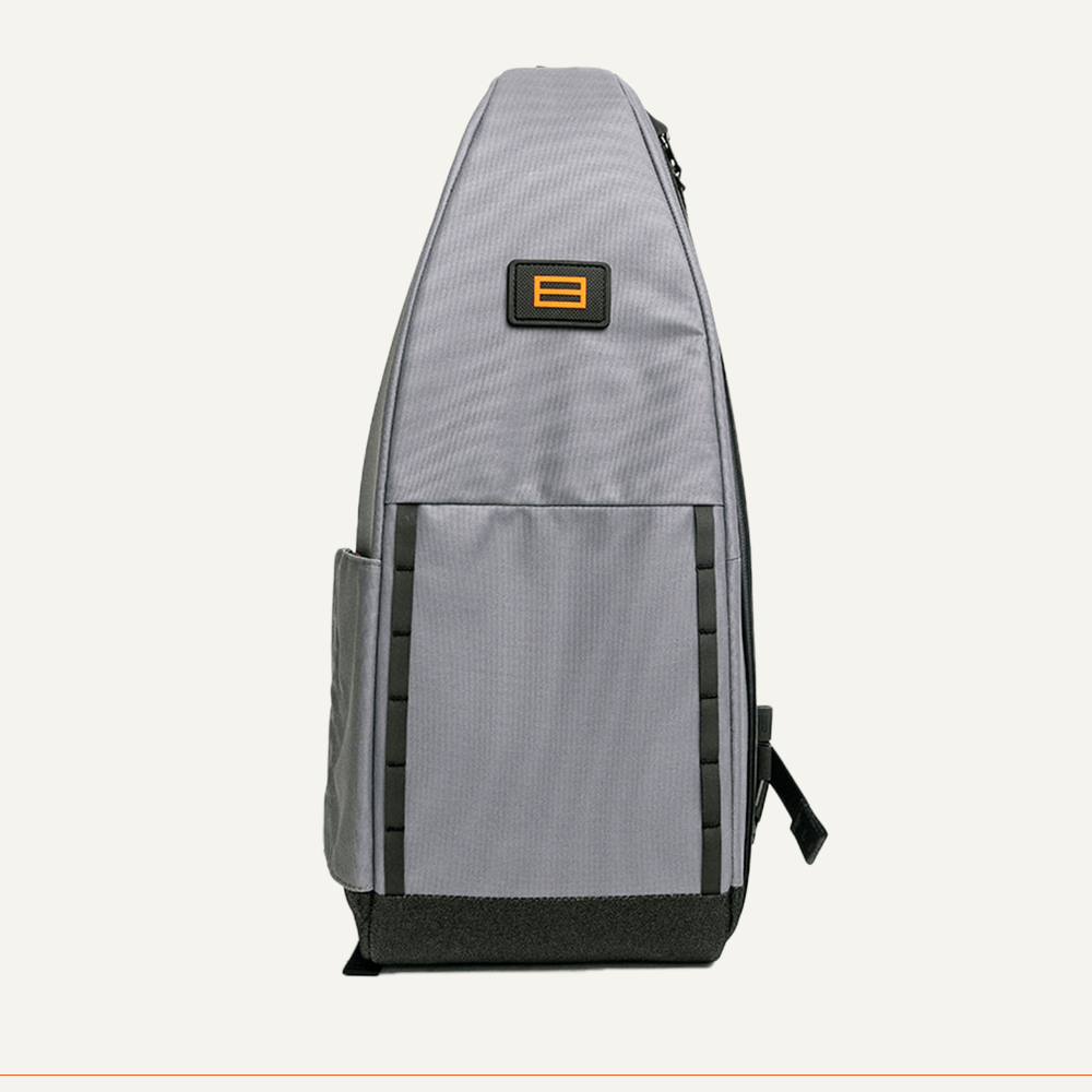 The FORWRD Cross Court Pickleball Sling is shown from the side in gray with a rectangular front pocket, black base, vertical zipper, yellow and black logo, and narrow slot pocket. Its lightweight, durable design is ideal as a pickleball bag.
