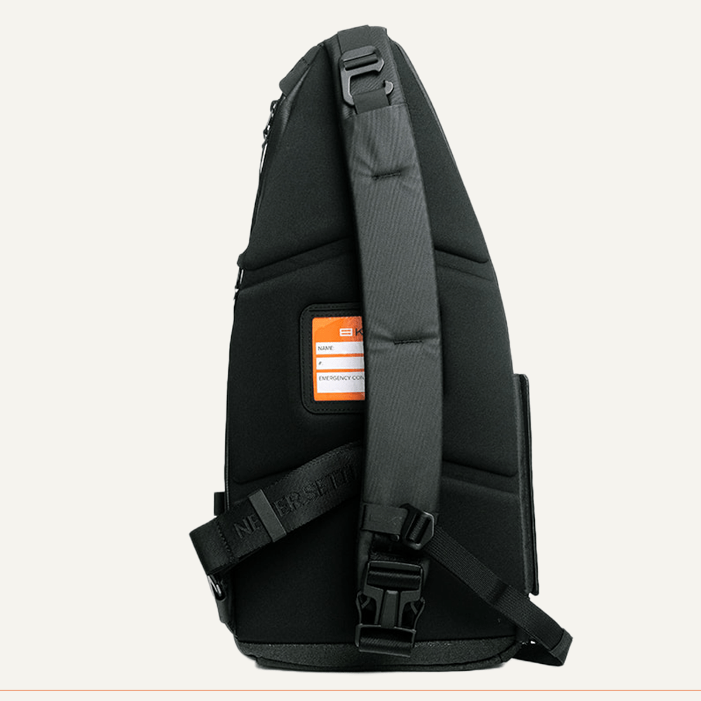 The FORWRD Cross Court Pickleball Sling is a black, triangular backpack with a thick padded adjustable strap, orange emergency contact label, angular stitching for structure, and a large buckle. Lightweight and durable for active players.