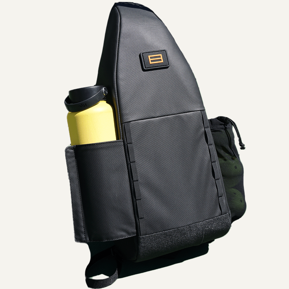 The FORWRD Cross Court Pickleball Sling is a sleek black diagonal backpack featuring a gold logo patch, side pocket with yellow water bottle, drawstring pocket, and lightweight durable design. Shown against a plain light background.