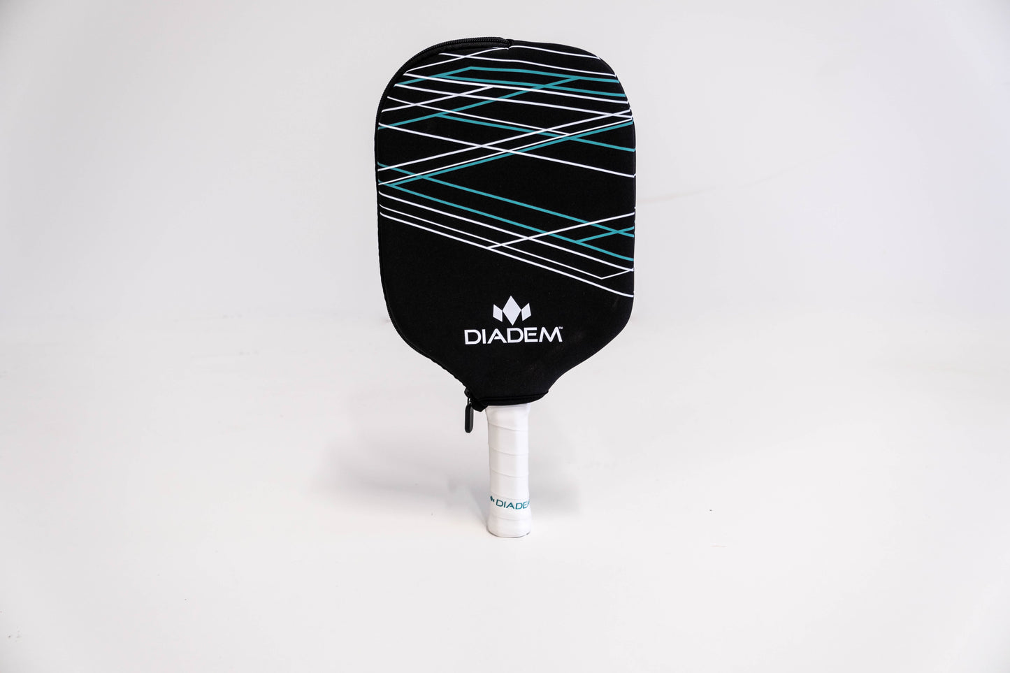 A black Diadem Sports pickleball paddle with white and teal lines stands upright, handle wrapped in white, next to the Diadem Paddle Cover featuring the Diadem logo and a white zipper, all set on a plain white background.